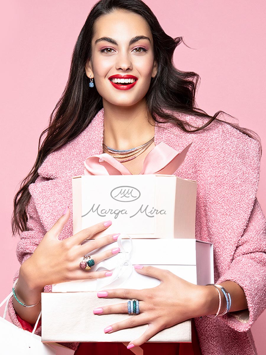 Hermosa mujer con joyas de lujo sostiene cajas de color blanco con regalos de Joyería Marga Mira. En las manos lleva brillantes anillos de lujo, a juego con pulseras y collares de joyería fina
