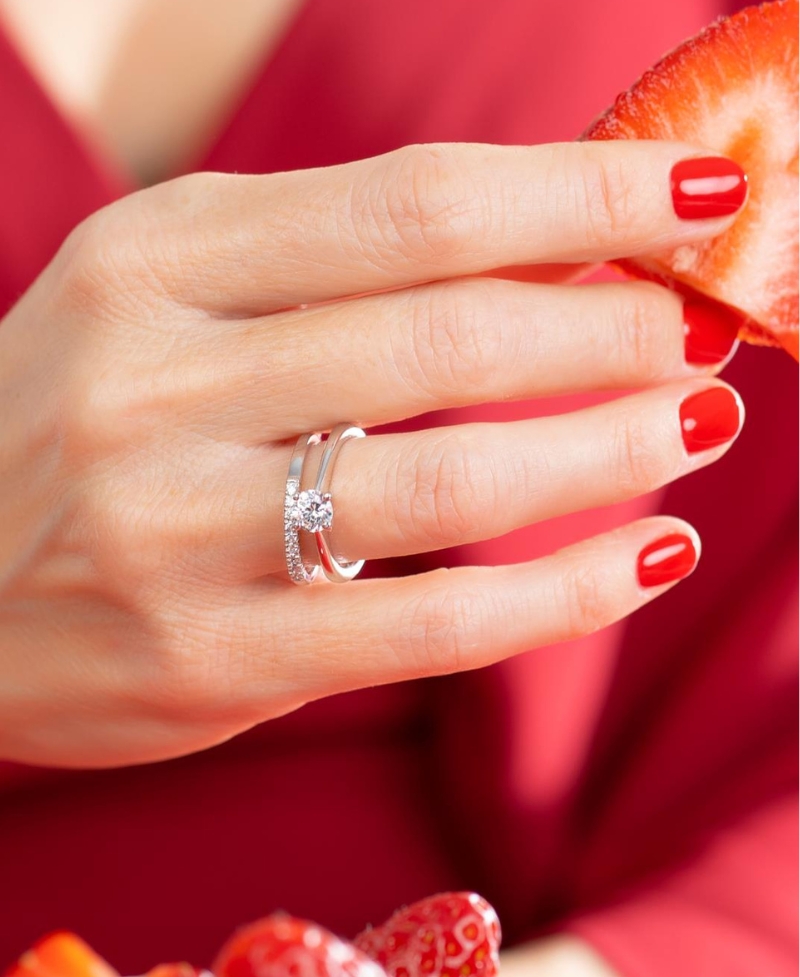 Elegante mano de mujer con anillos de diamantes sosteniendo unas fresas jugosas. Las uñas y el vestido son de color rojo, evocando las tonalidades del amor en san valentin y los regalos de lujo disponibles en joyeria marga mira